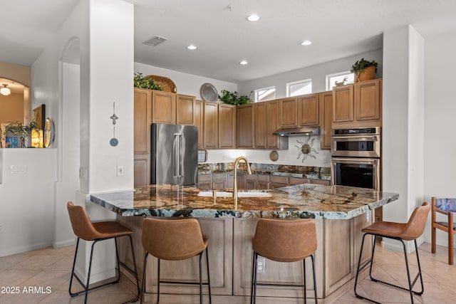 kitchen featuring stainless steel appliances, dark stone counters, sink, a breakfast bar, and light tile patterned floors