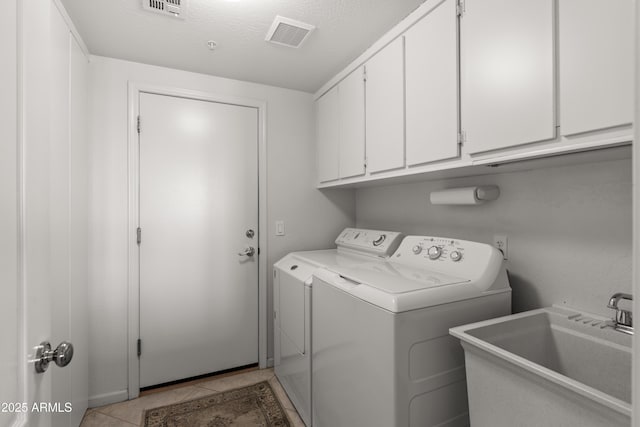 laundry room with light tile patterned floors, a textured ceiling, washing machine and dryer, cabinets, and sink