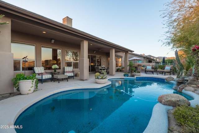 pool at dusk featuring ceiling fan and a patio area