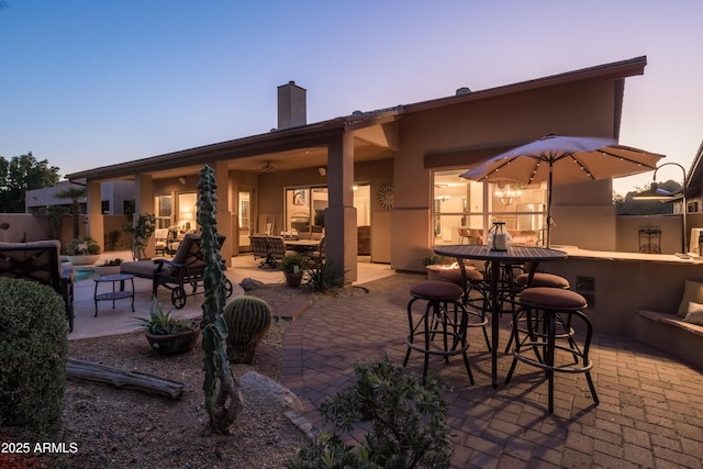 patio terrace at dusk featuring ceiling fan and exterior bar