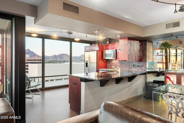 kitchen with sink, tasteful backsplash, dark stone counters, appliances with stainless steel finishes, and a kitchen bar