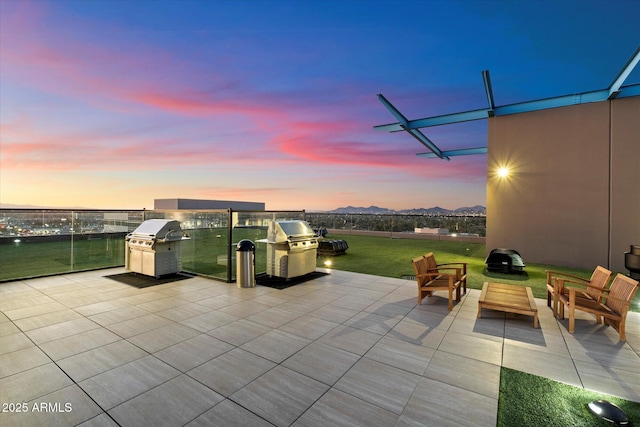 patio terrace at dusk featuring a mountain view, area for grilling, and a lawn