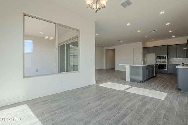 kitchen with appliances with stainless steel finishes, light wood-type flooring, a kitchen island with sink, sink, and a chandelier