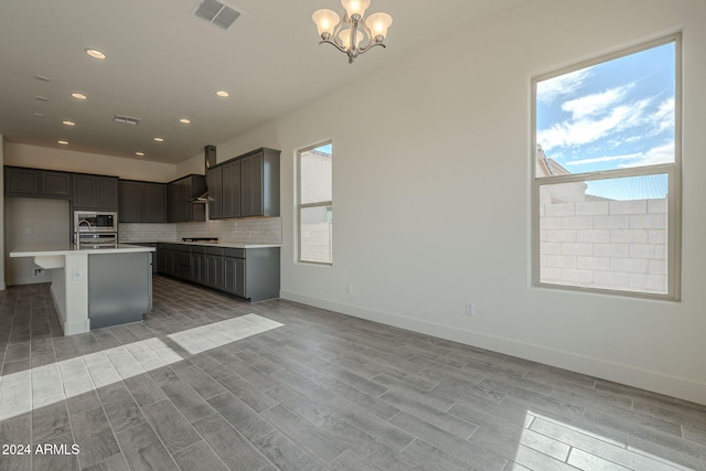 kitchen with stainless steel microwave, a kitchen island with sink, light hardwood / wood-style flooring, and pendant lighting