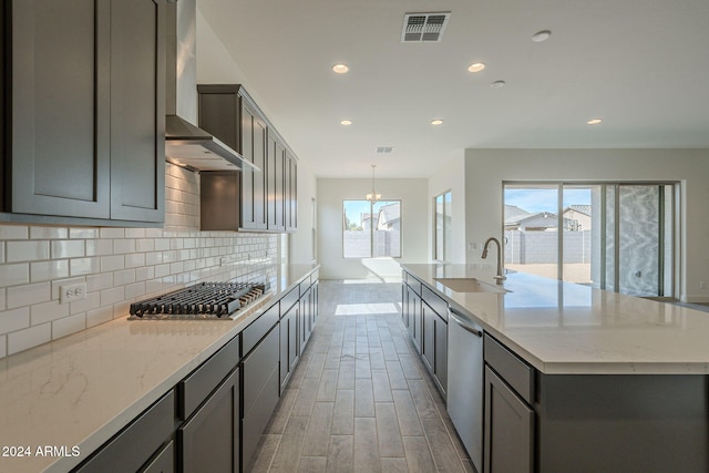 kitchen with gray cabinetry, sink, wall chimney exhaust hood, light hardwood / wood-style flooring, and an island with sink