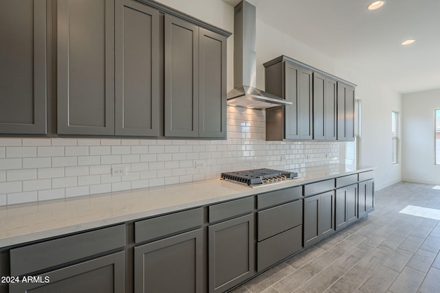 kitchen with gray cabinetry, light stone counters, wall chimney exhaust hood, and stainless steel gas stovetop