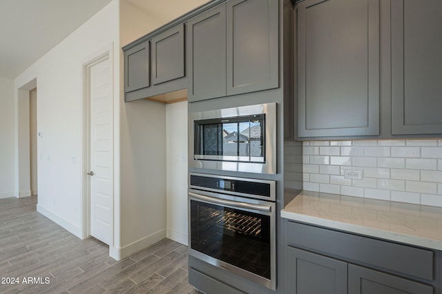 kitchen featuring appliances with stainless steel finishes, light wood-type flooring, light stone counters, and gray cabinetry