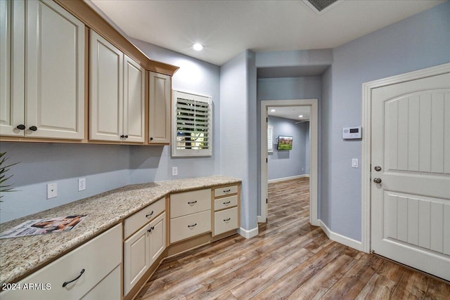 kitchen featuring cream cabinets, light hardwood / wood-style flooring, and light stone counters