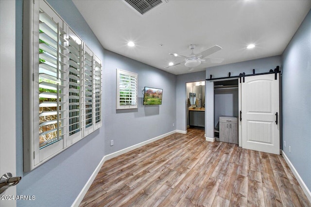 unfurnished bedroom with ensuite bath, ceiling fan, light wood-type flooring, and a barn door