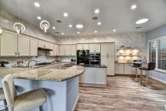 kitchen featuring kitchen peninsula, light stone countertops, black appliances, light hardwood / wood-style flooring, and hanging light fixtures