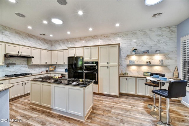 kitchen with decorative backsplash, light wood-type flooring, black appliances, dark stone countertops, and a center island