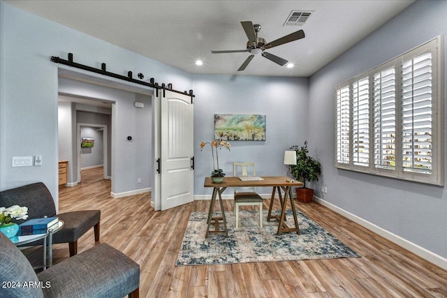 office with ceiling fan, light wood-type flooring, and a barn door