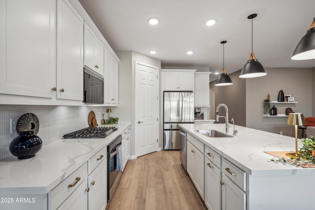 kitchen featuring appliances with stainless steel finishes, sink, decorative light fixtures, white cabinets, and an island with sink