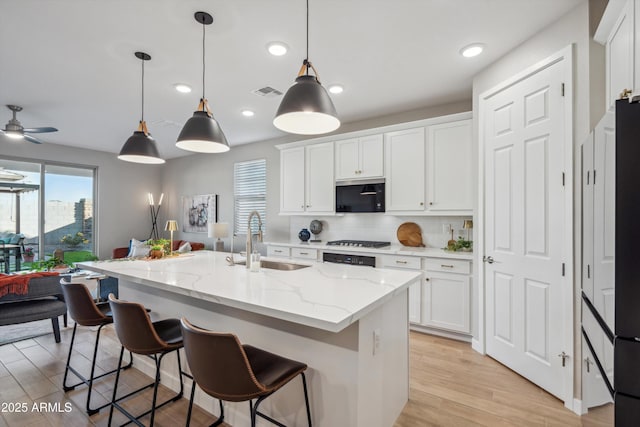 kitchen featuring ceiling fan, sink, white cabinetry, hanging light fixtures, and an island with sink