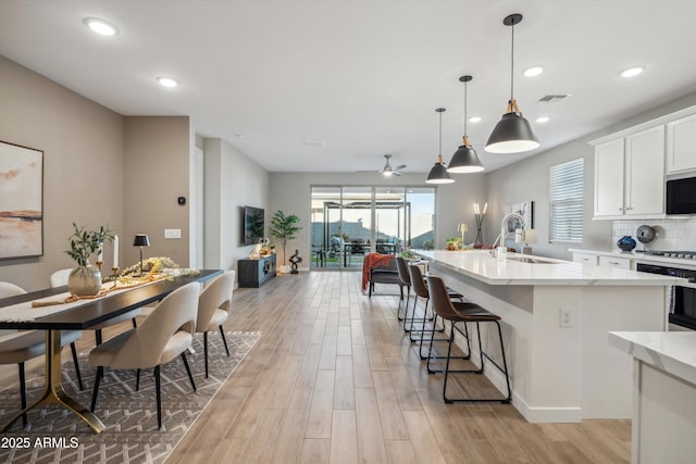 kitchen featuring white cabinetry, sink, ceiling fan, an island with sink, and decorative light fixtures