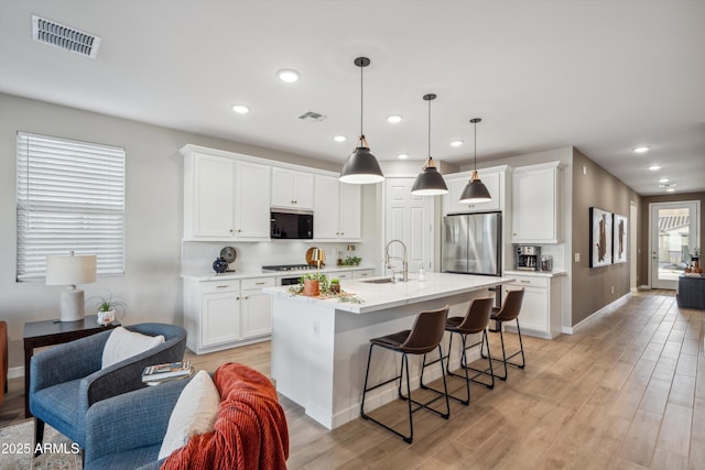 kitchen featuring white cabinets, a center island with sink, and stainless steel appliances