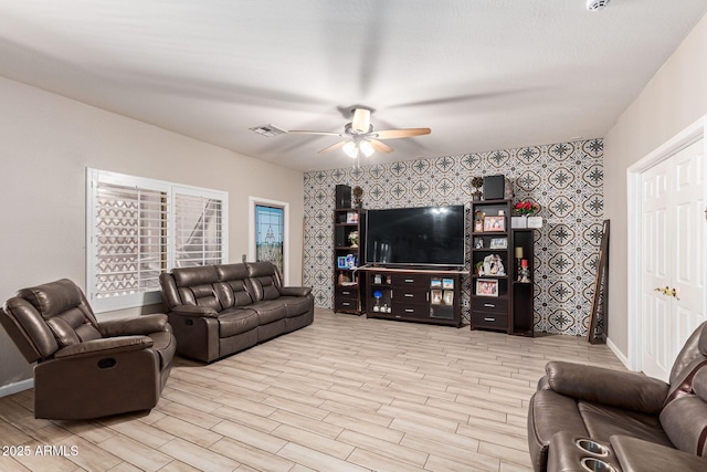 living area with wood finish floors, visible vents, an accent wall, a ceiling fan, and baseboards