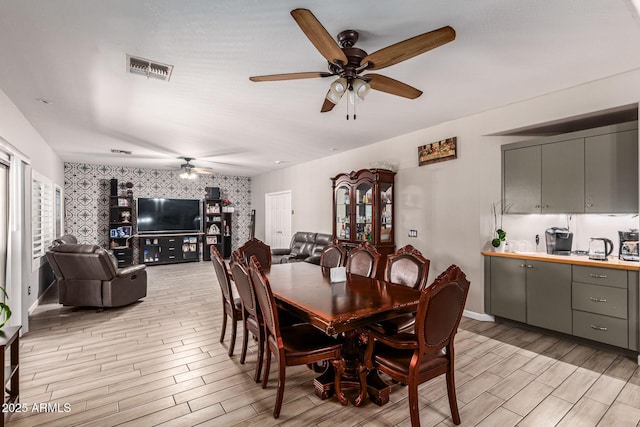 dining area featuring visible vents, wood tiled floor, ceiling fan, baseboards, and wallpapered walls