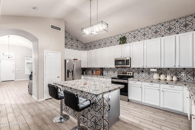 kitchen with arched walkways, a chandelier, white cabinetry, appliances with stainless steel finishes, and pendant lighting