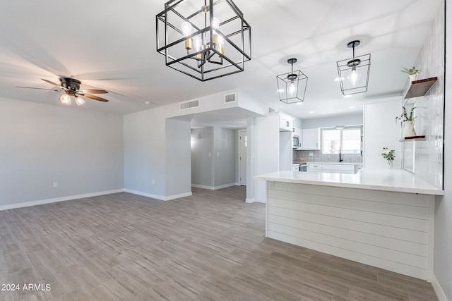 kitchen featuring white cabinets, hardwood / wood-style flooring, decorative light fixtures, ceiling fan with notable chandelier, and kitchen peninsula