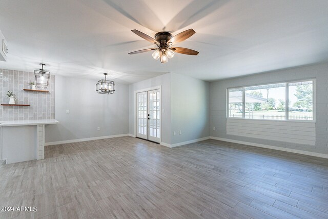 unfurnished living room with ceiling fan with notable chandelier, french doors, and light hardwood / wood-style floors