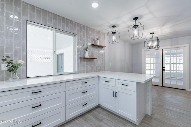 kitchen featuring white cabinets, light stone countertops, light hardwood / wood-style floors, kitchen peninsula, and pendant lighting