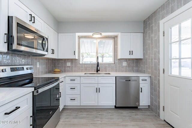 kitchen featuring backsplash, stainless steel appliances, sink, light wood-type flooring, and white cabinets