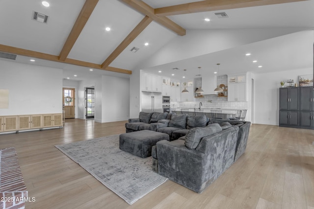 living room featuring beamed ceiling, high vaulted ceiling, sink, and light hardwood / wood-style floors