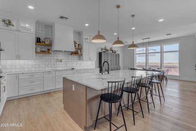 kitchen featuring pendant lighting, a breakfast bar, light stone countertops, white cabinets, and a center island with sink