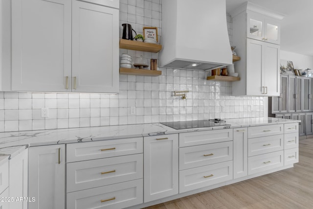 kitchen with custom exhaust hood, light stone countertops, black electric stovetop, and white cabinets