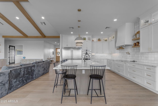 kitchen with white cabinetry, appliances with stainless steel finishes, a kitchen island with sink, and custom exhaust hood