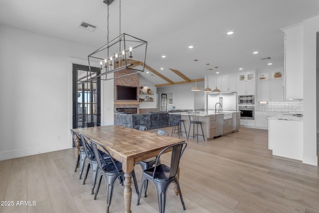 dining room featuring vaulted ceiling, sink, a fireplace, and light hardwood / wood-style floors