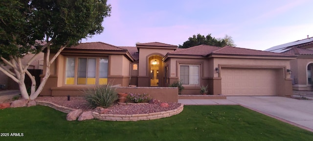 mediterranean / spanish home featuring a tiled roof, stucco siding, a front yard, a garage, and concrete driveway