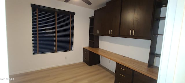 unfurnished office with light wood-style floors, ceiling fan, built in study area, and baseboards