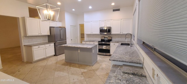 kitchen featuring visible vents, a sink, appliances with stainless steel finishes, a kitchen island, and light stone counters