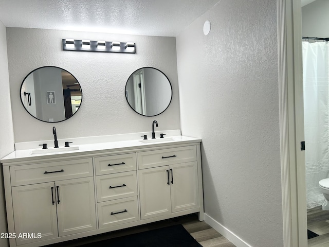 full bathroom with wood finished floors, a textured wall, and a sink