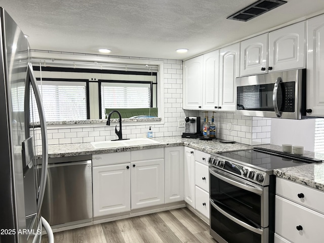 kitchen featuring visible vents, light wood-style flooring, stainless steel appliances, white cabinetry, and a sink