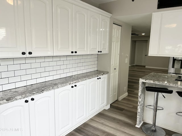 kitchen with backsplash, baseboards, light stone countertops, wood finished floors, and white cabinetry