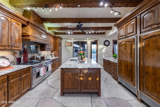 kitchen featuring decorative backsplash, light stone counters, double oven range, and an island with sink