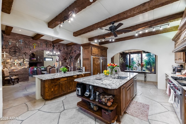 kitchen with beam ceiling, sink, stainless steel appliances, a center island with sink, and ceiling fan with notable chandelier