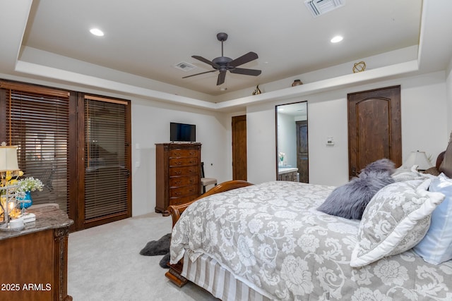 bedroom with a raised ceiling, ensuite bath, ceiling fan, and light carpet