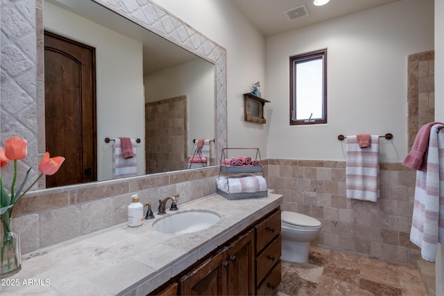 bathroom featuring vanity, tile walls, and toilet