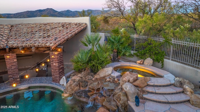 pool at dusk with a mountain view and an in ground hot tub