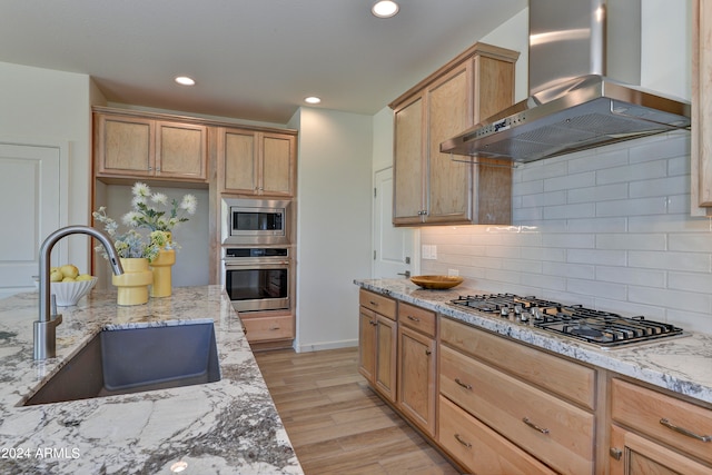 kitchen with light wood-type flooring, light stone counters, wall chimney exhaust hood, sink, and appliances with stainless steel finishes