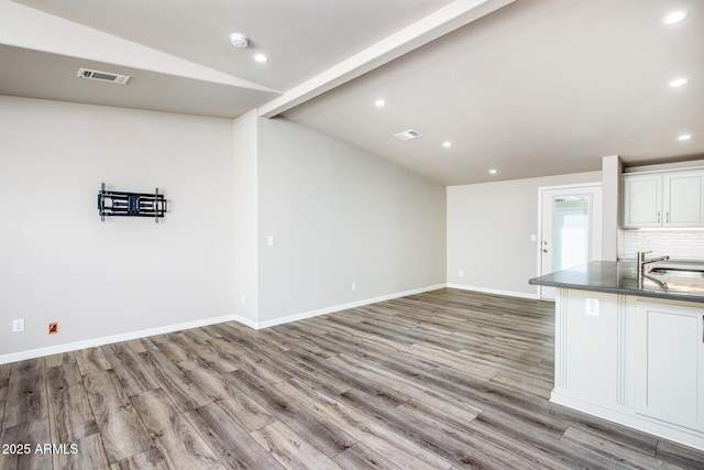 kitchen with a sink, wood finished floors, visible vents, baseboards, and backsplash