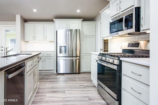 kitchen with appliances with stainless steel finishes, light wood-type flooring, a sink, and tasteful backsplash