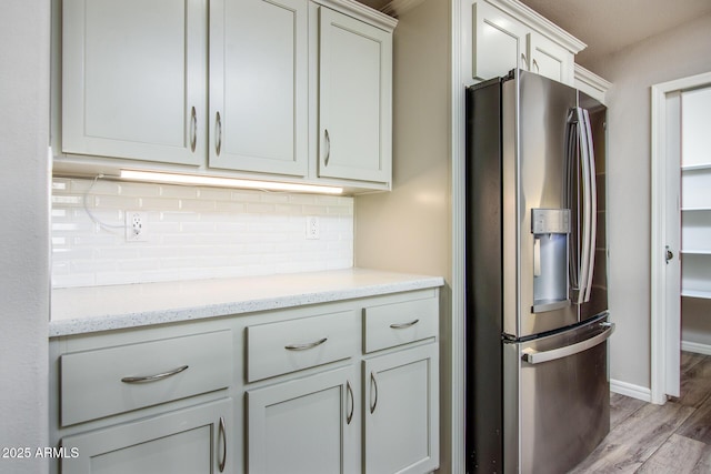 kitchen with light wood finished floors, stainless steel fridge, tasteful backsplash, baseboards, and light stone counters