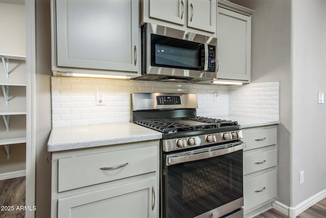 kitchen with baseboards, decorative backsplash, appliances with stainless steel finishes, dark wood-type flooring, and light stone countertops