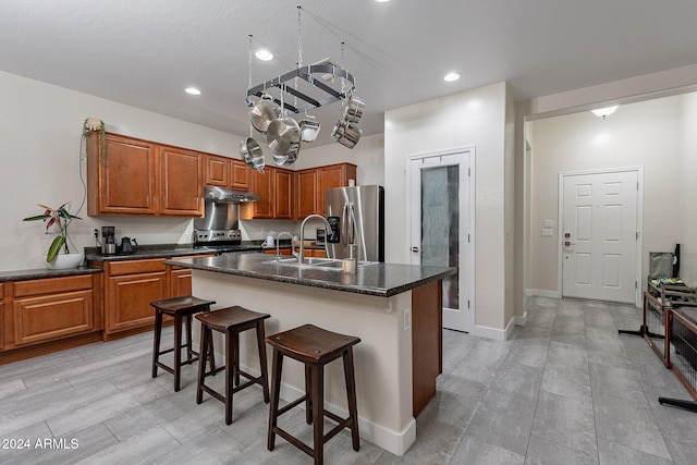 kitchen featuring appliances with stainless steel finishes, a breakfast bar, sink, dark stone counters, and a center island with sink