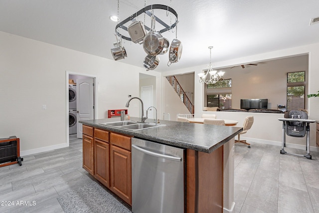 kitchen with sink, stacked washer and clothes dryer, an island with sink, decorative light fixtures, and stainless steel dishwasher